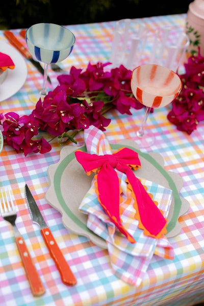 Colorful table setting with plaid tablecloth, pink napkin, and vibrant flowers.