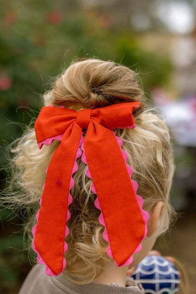 Person with a large red bow in their hair against a blurred outdoor background