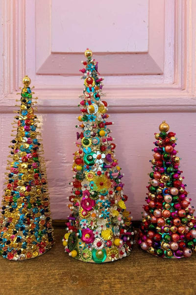 Three colorful beaded Christmas trees on a wooden surface with a pink wall background.