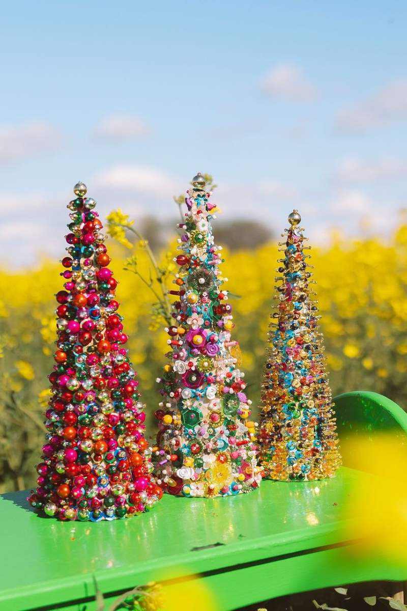 Three colorful beaded Christmas trees on a green surface with a yellow floral background