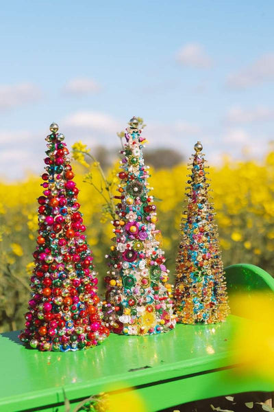 Three colorful beaded Christmas trees on a green surface with a yellow floral background