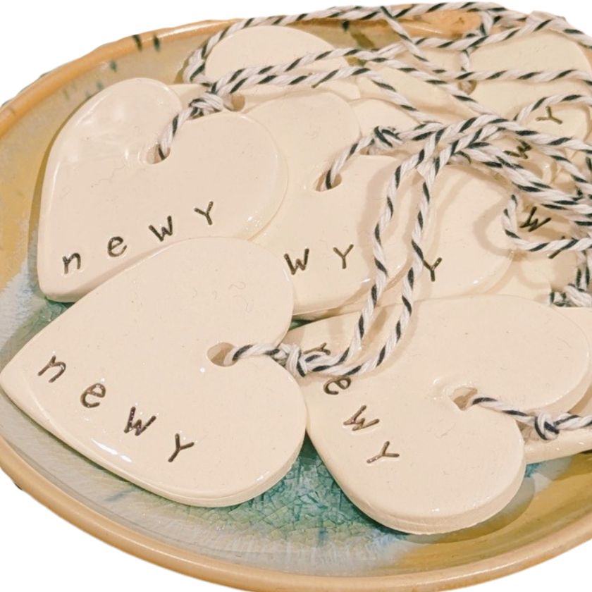 Newy Heart Tag by Caroline C with small ribbon. Made from ceramic with NEWY printed on the edge.