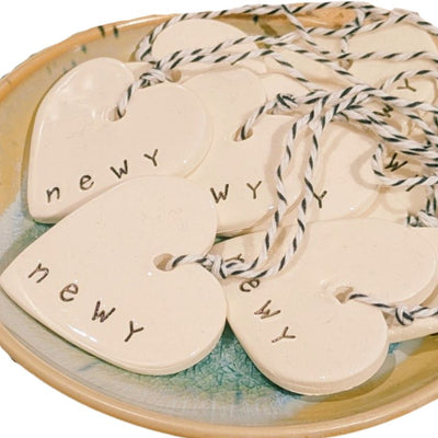 Newy Heart Tag by Caroline C with small ribbon. Made from ceramic with NEWY printed on the edge.