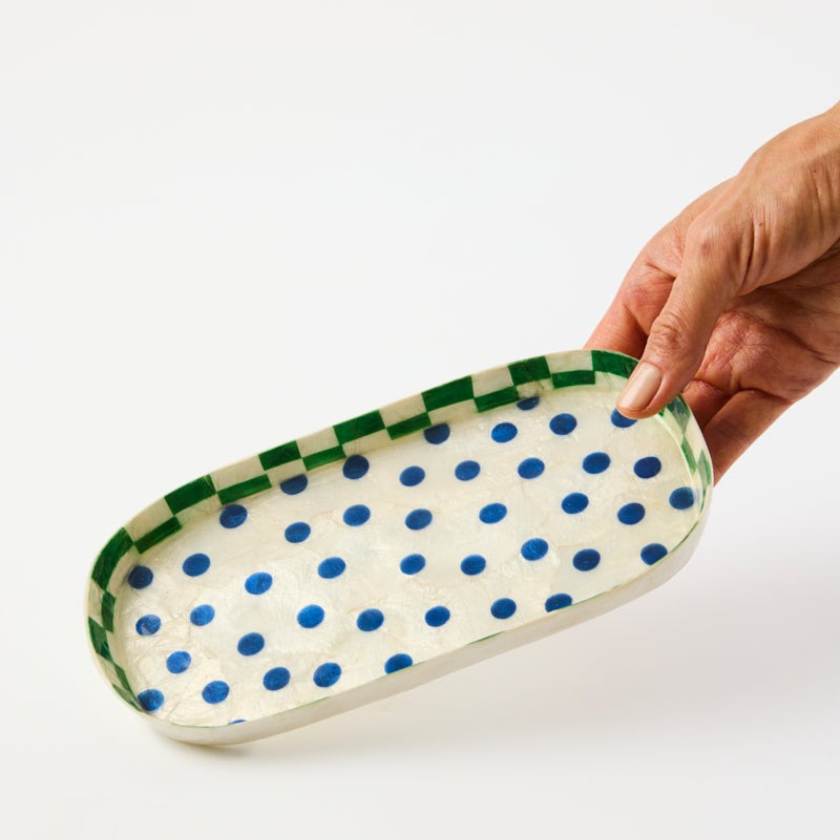 Hand holding a tray with blue polka dots and green rim on a white background