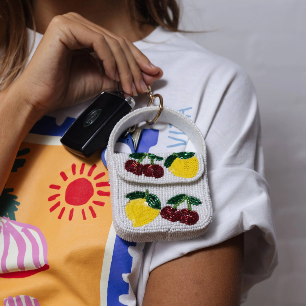 Person holding a small handbag with fruit designs against a colorful background by Zoda