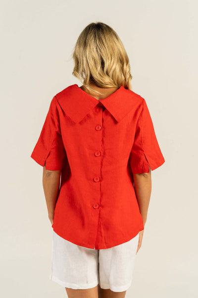 A woman exudes confidence in a vibrant red cowl neck top with medium sleeves and button back detailing.