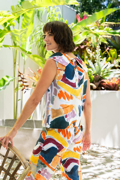 Woman wearing a colorful sleeveless top and pants standing among plants.