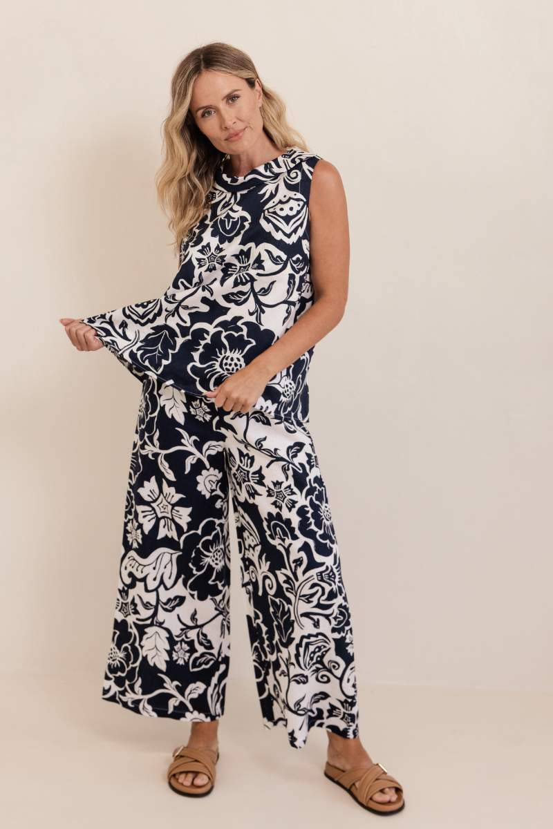 Woman wearing a navy and white floral pants and top on a plain background