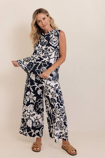 Woman wearing a navy and white floral pants and top on a plain background