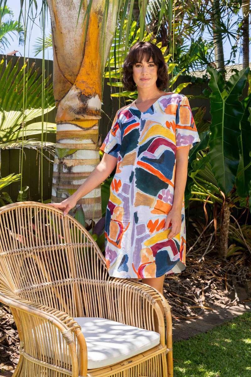 Woman in a colourful dress standing next to a wicker chair in a garden setting