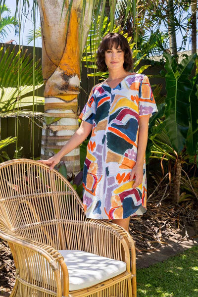Woman in a colourful dress standing next to a wicker chair in a garden setting