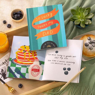 Greeting cards on a table with a 'So lucky you're my dad' card and a cake illustration card.