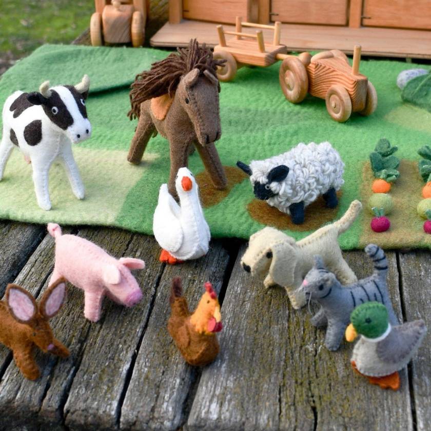 Collection of felt farm animals on a wooden surface with a green blanket and wooden toys in the background.