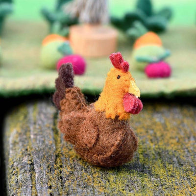 Felted rooster figurine on a textured surface with a blurred colorful background
