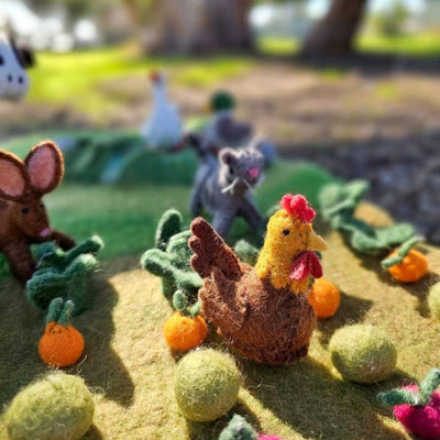 Felt animal toys on a grassy patch with pumpkins and flowers.