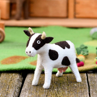 Felt cow toy on a wooden surface with a farm-themed background