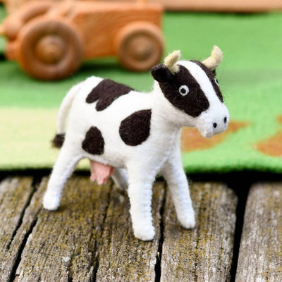 Small cow toy on a wooden surface with a colorful blanket in the background