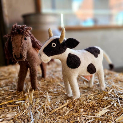 Felt horse and cow toys on a bed of straw with a blurred indoor background