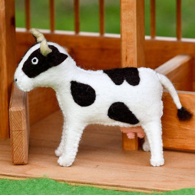 Black and white toy cow on a wooden platform with a grassy background