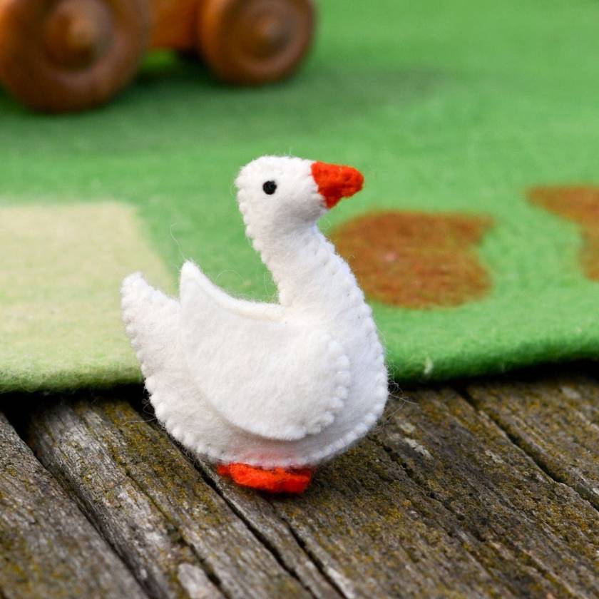 White toy goose with red beak and feet on a wooden surface