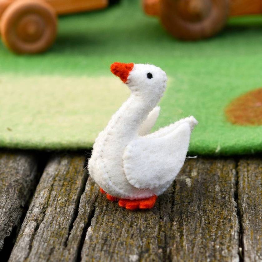 White goose figurine with orange beak and feet on a wooden surface with a green fabric background.
