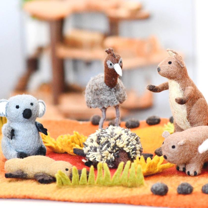 Felt animal toys on a fabric surface with blurred wooden furniture in the background