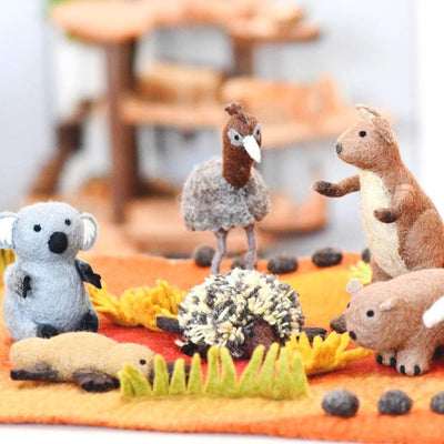 Felt animal toys on a fabric surface with blurred wooden furniture in the background