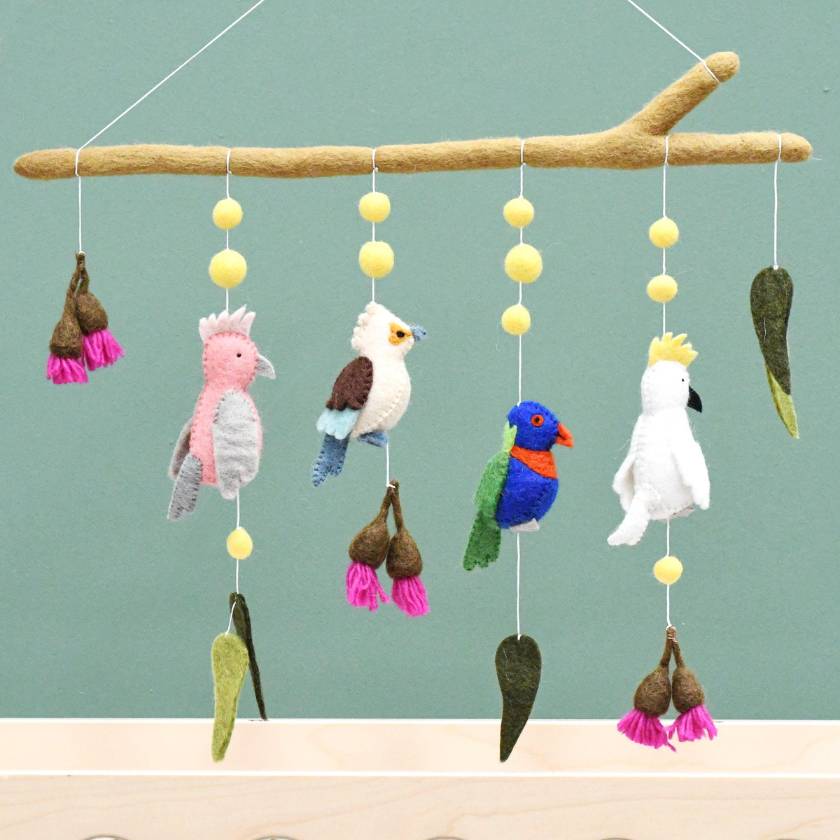 Colorful bird-themed mobile with hanging toys on a branch against a light blue background