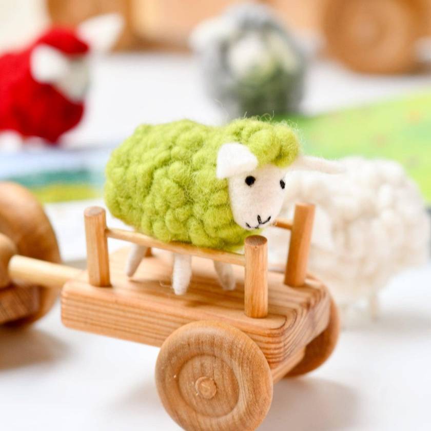 Toy sheep with green wool on a wooden cart, blurred background