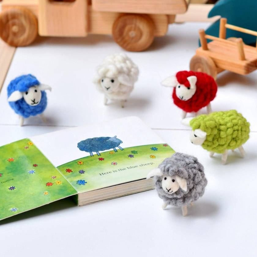 Colorful toy sheep figures with a book on a white surface