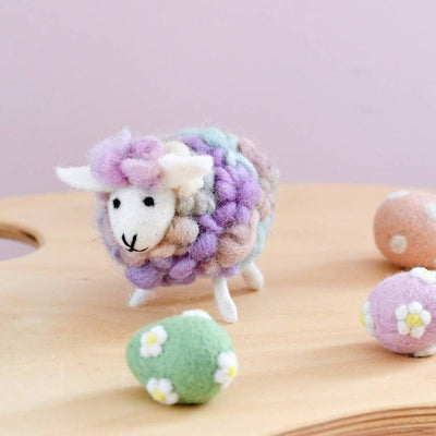 Colorful felted sheep toy on a wooden surface with a light purple background