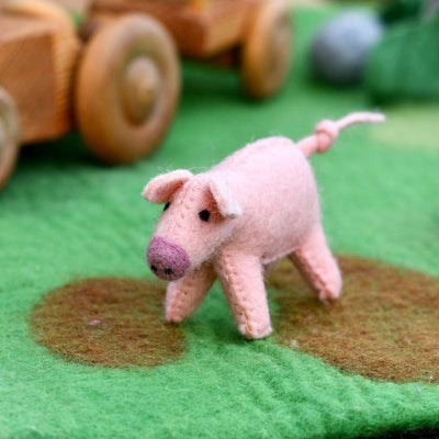 Pink toy pig on a green surface with wooden wheels in the background