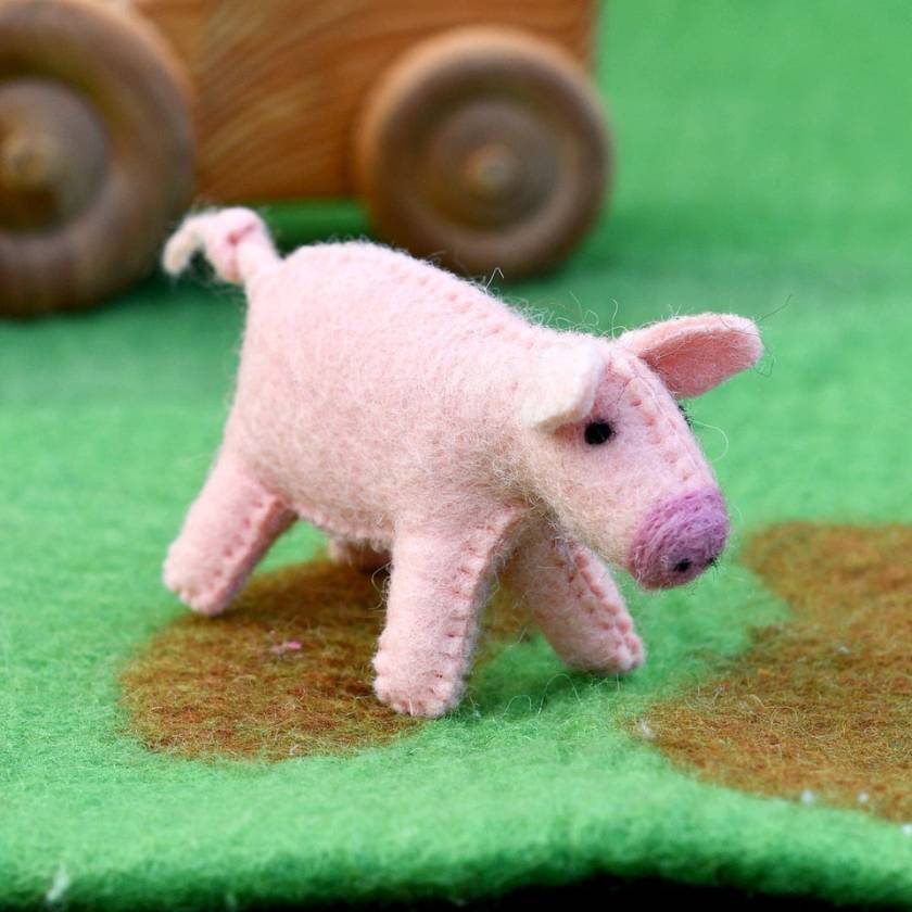 Pink felt pig toy on a green surface with wooden wheels in the background