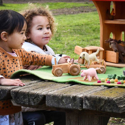 Two children playing with wooden toys on a wooden table outdoors.