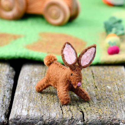 Small brown felt bunny toy on a wooden surface with Easter decorations in the background.