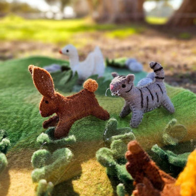 Felt animal toys on a textured landscape with a duck in the background