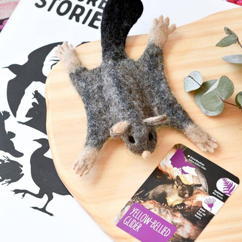 Felted yellow-bellied glider toy on a person's arm with educational card in the background