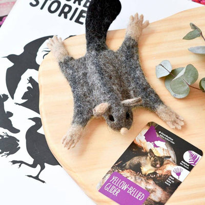 Felted yellow-bellied glider toy on a person's arm with educational card in the background